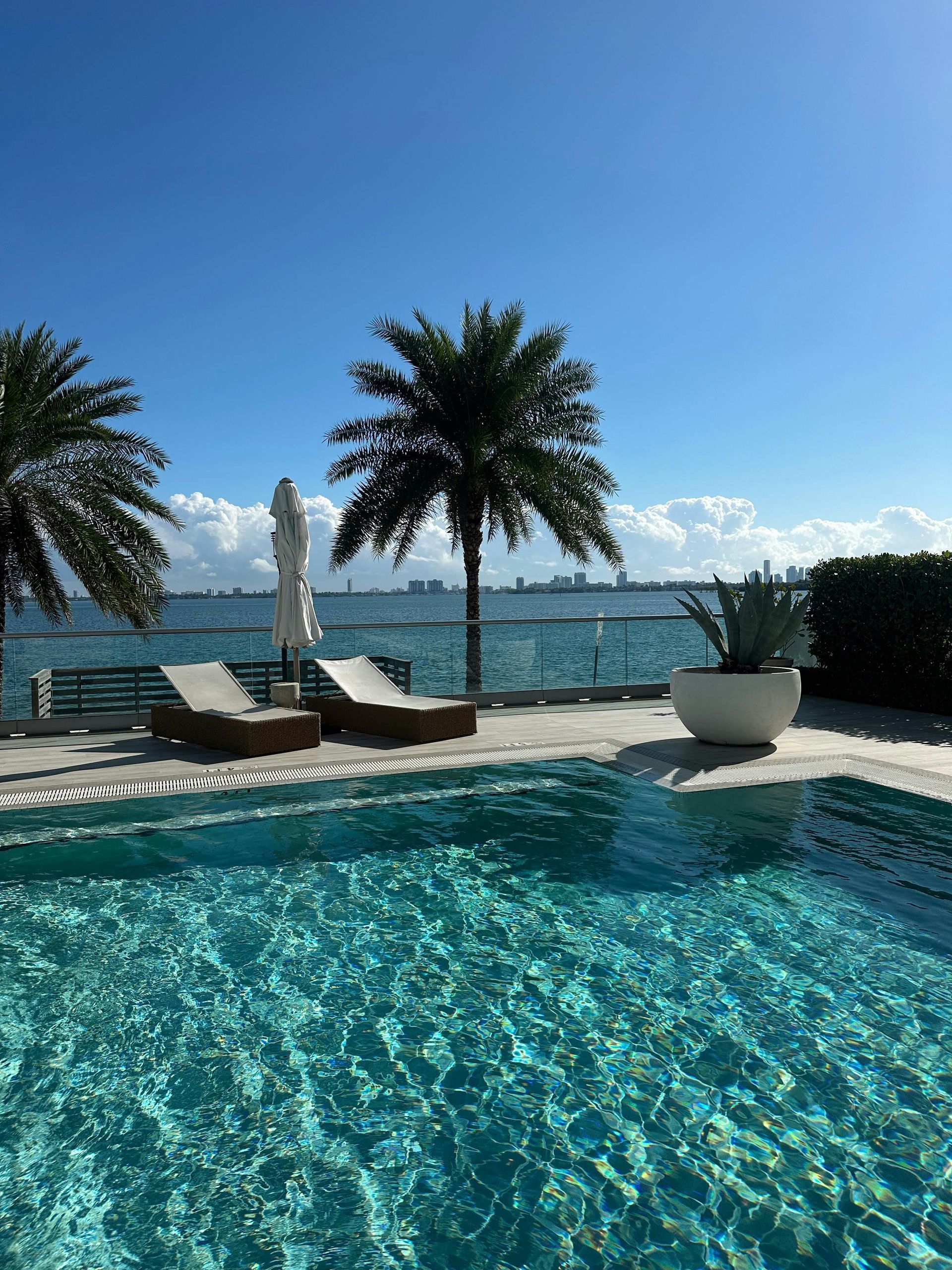 Tropical pool with turquoise water, palm trees, lounge chairs, and ocean view under a clear blue sky