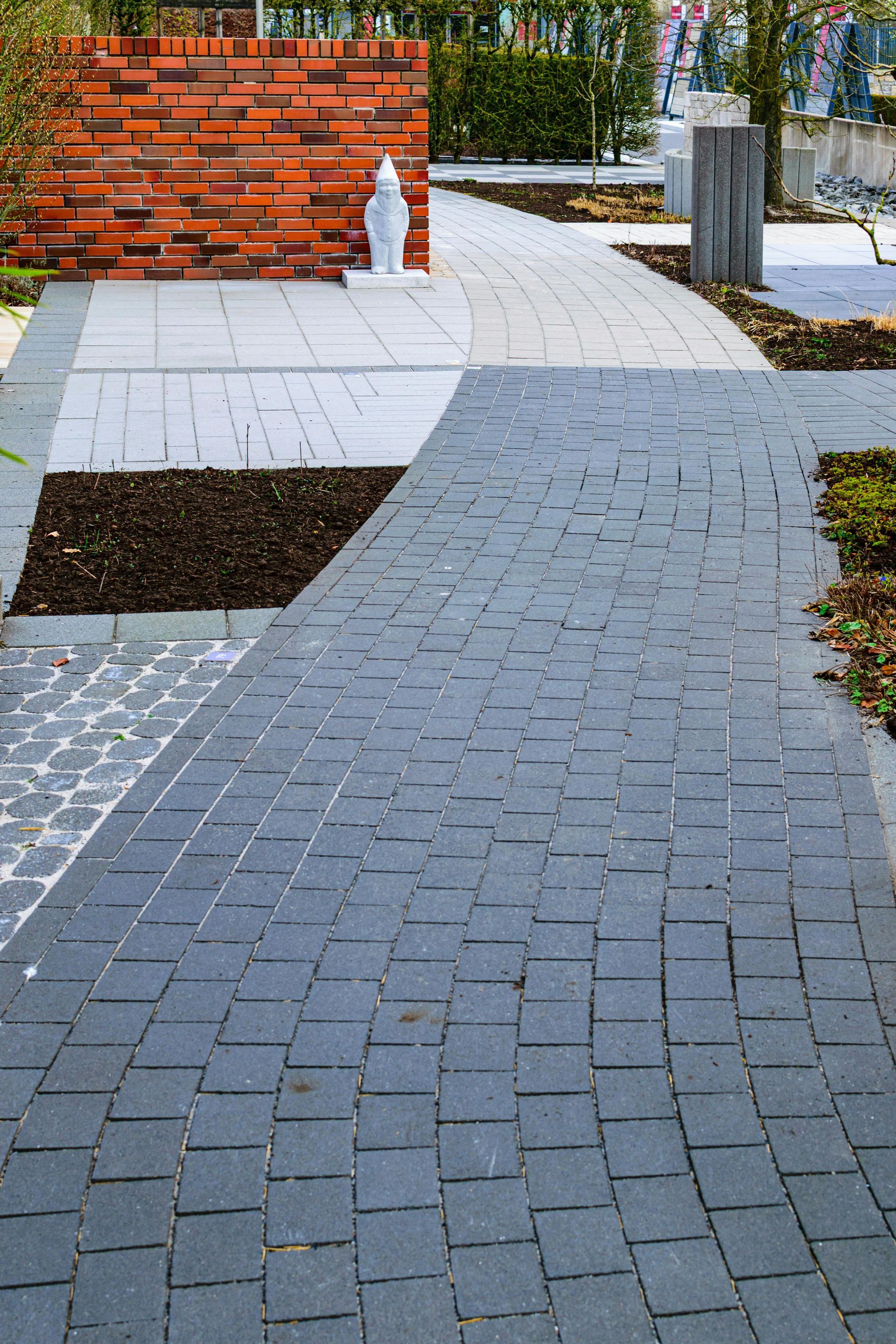 Brick-and-gray paver walkway beside a red brick wall and small snowy patches