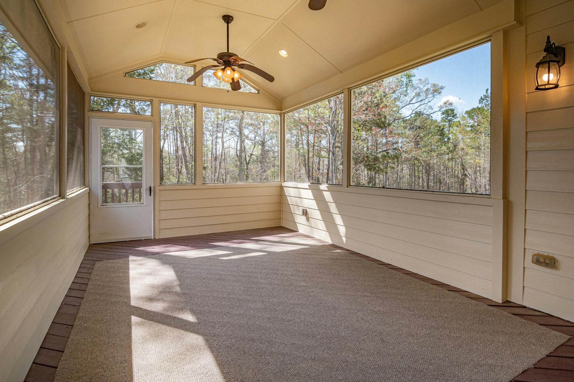 Sunroom with large windows, carpeted floor, ceiling fan, and sunlight streaming in.