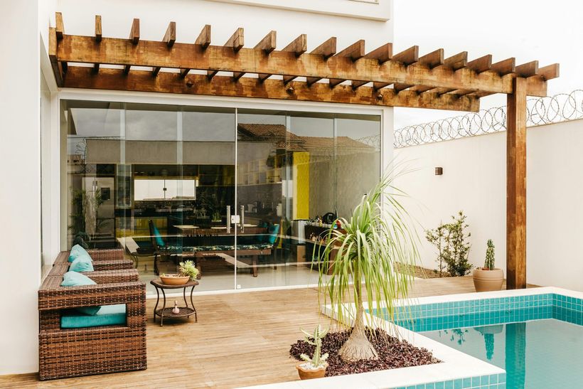 Modern patio with glass sliding doors, wooden pergola, seating, and a turquoise pool