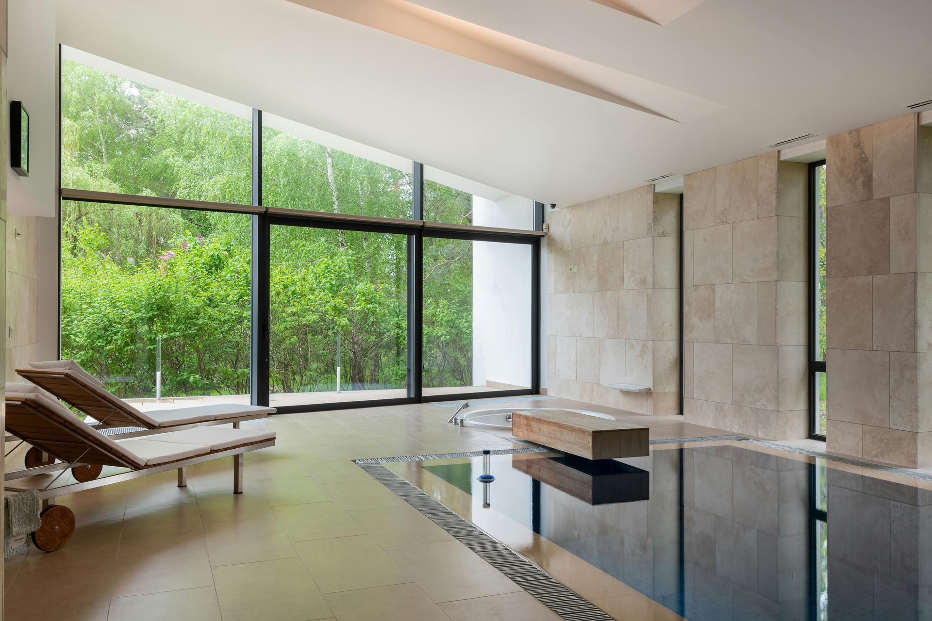 Modern spa interior with lounge chairs, large windows, stone walls, and an indoor pool