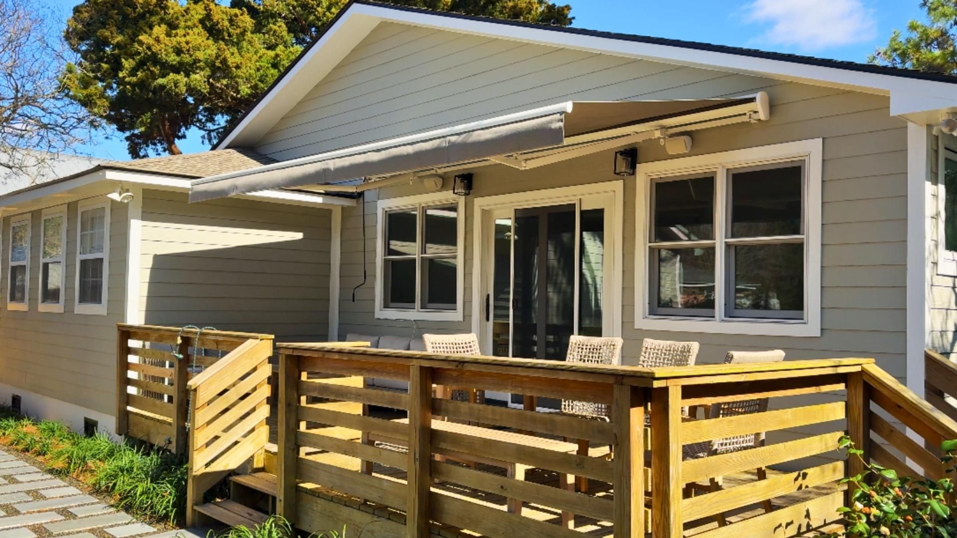 A wooden deck with a house; a tan retractable awning shades the sliding glass door.
