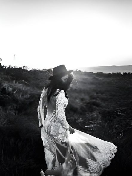 a woman in a white dress and hat is standing in a field .