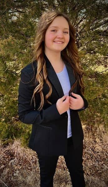 womain in black suit coat standing in front of tree