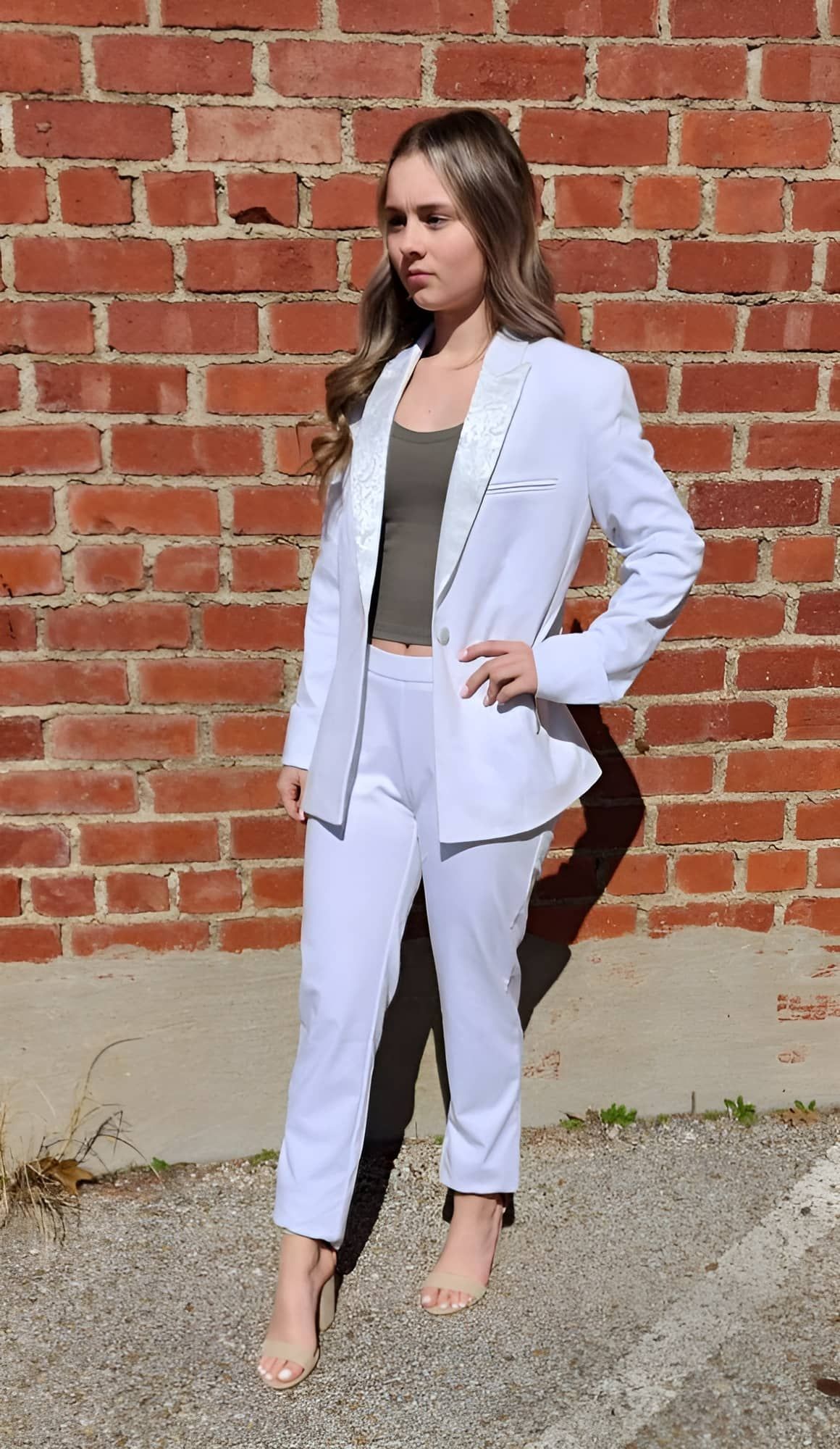 a woman in a white suit is standing in front of a brick wall .