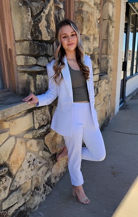 a woman in a white suit is leaning against a stone wall .