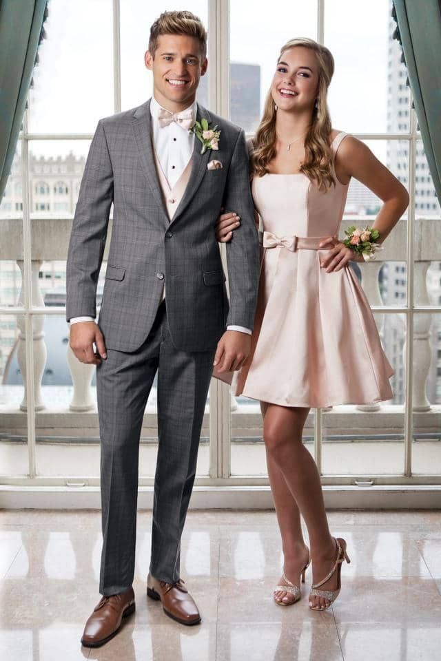 a man in a suit and a woman in a pink dress are standing next to each other in front of a window .