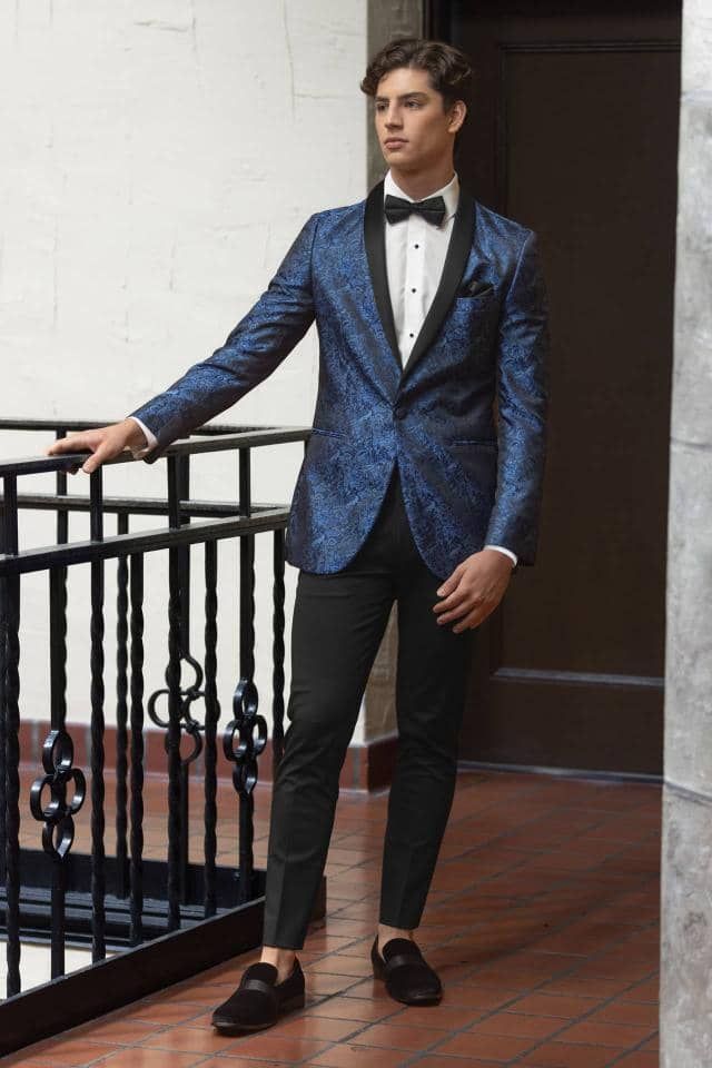 a man in a blue tuxedo and black pants is standing next to a railing .
