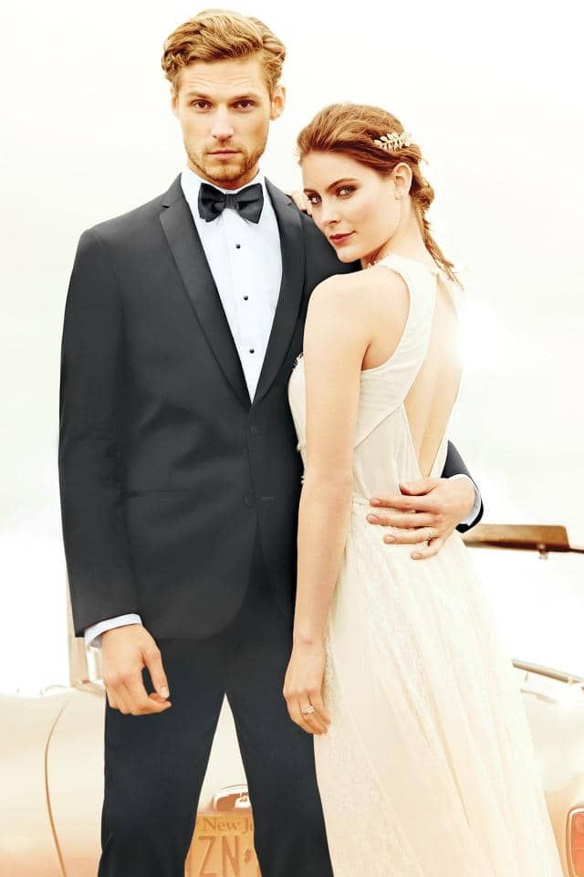a man in a tuxedo is standing next to a woman in a white dress .