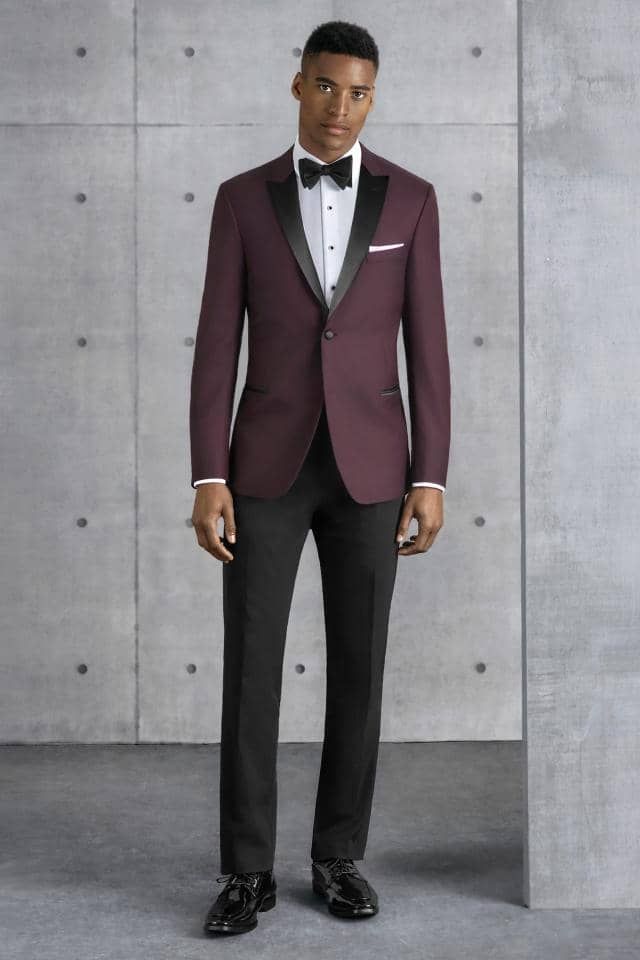 a man is wearing a burgundy tuxedo and black pants .