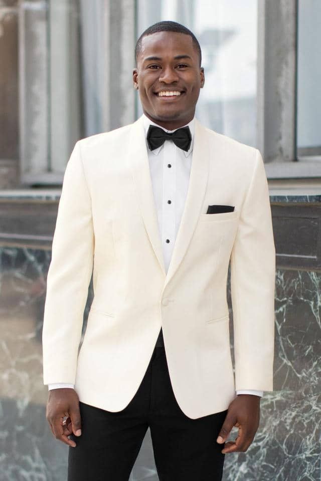 a man in a white tuxedo and black pants is smiling .
