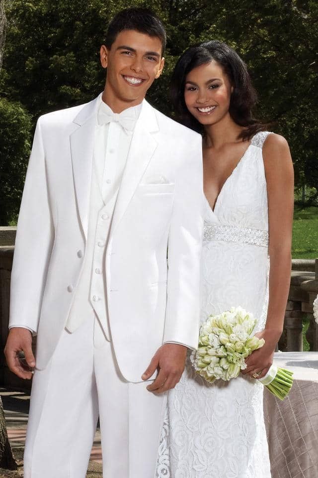a man in a white suit and a woman in a white dress are posing for a picture .