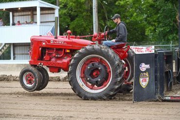 Red tractor pulling a sled on a dirt track, driven by a person in a cap
