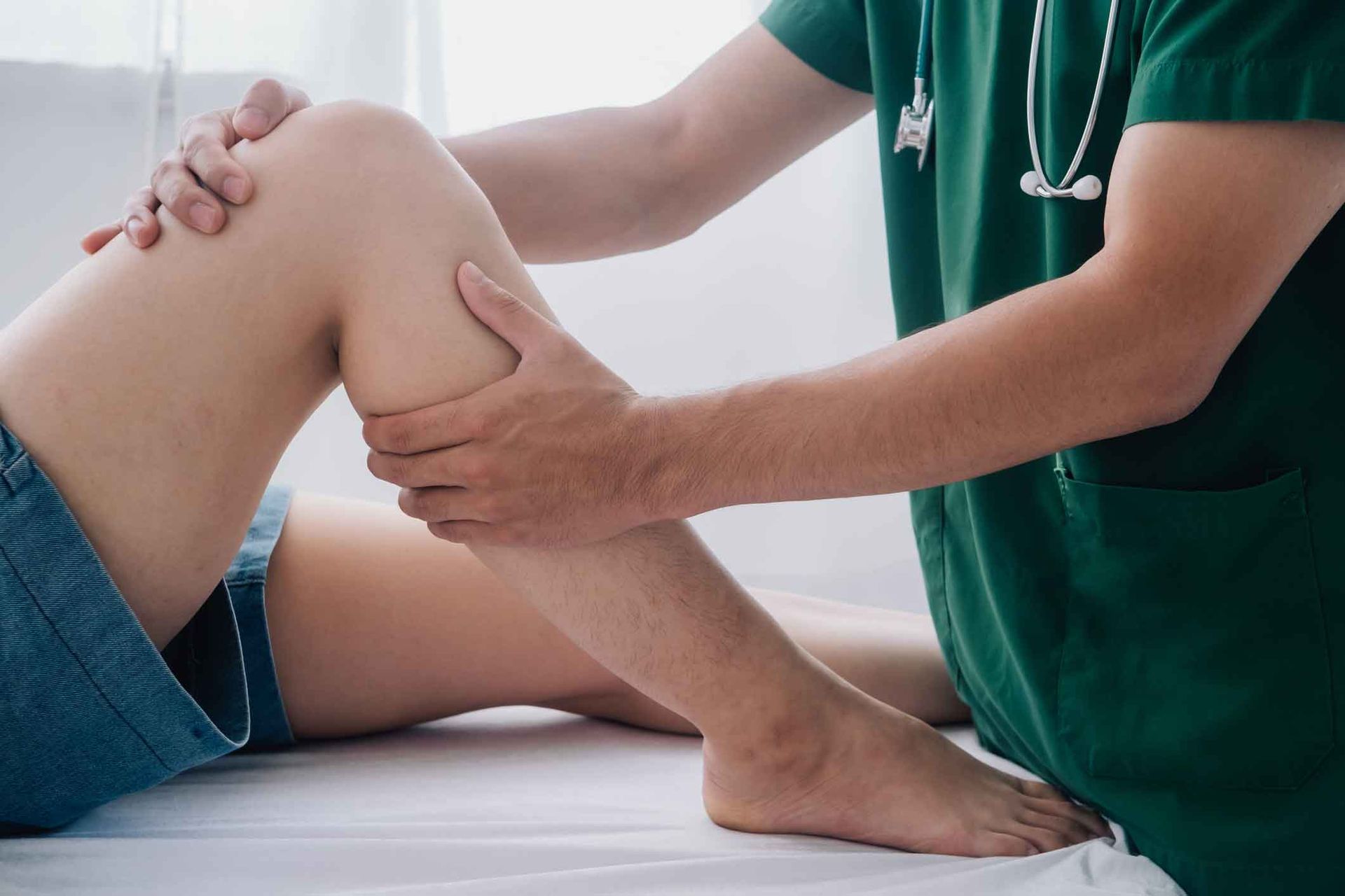 A doctor is examining a patient 's knee on a bed.