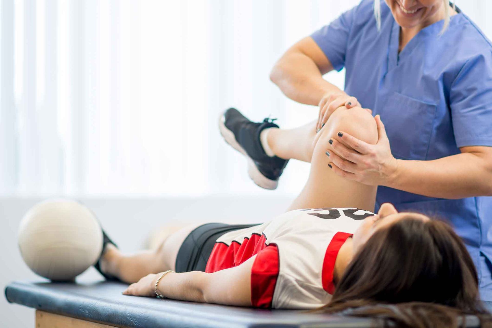 A woman is laying on a table getting her knee examined by a nurse.
