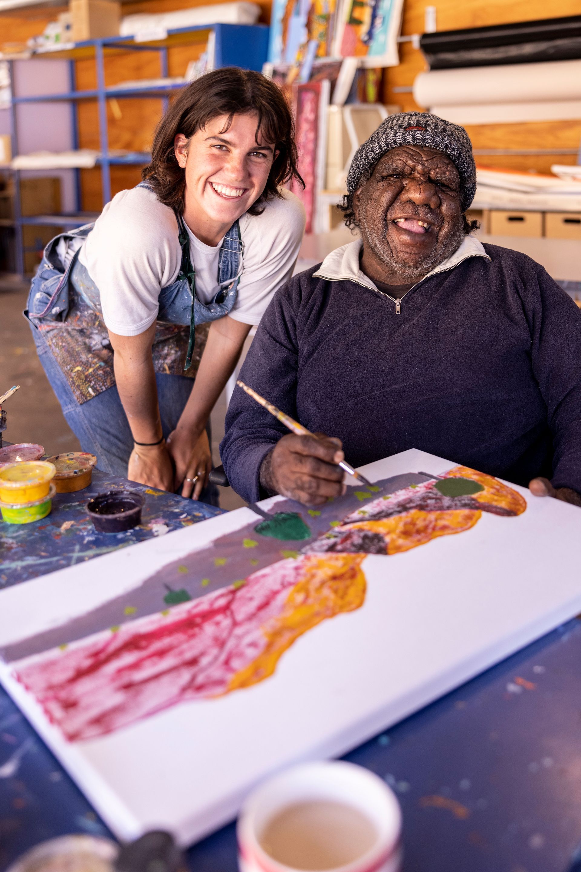 A woman is standing next to a man painting on a canvas.