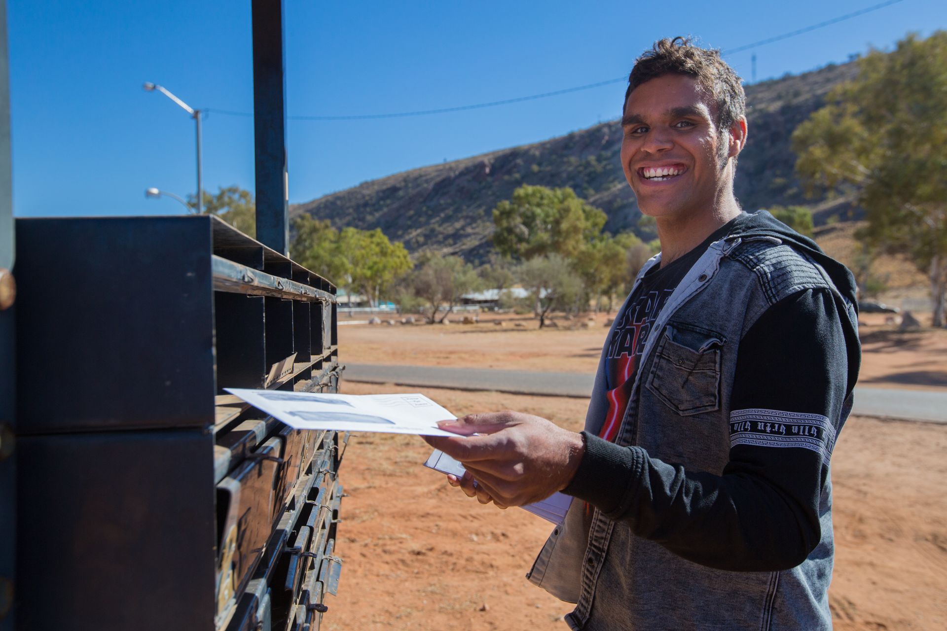 A man is smiling while holding a piece of paper in front of a mailbox.