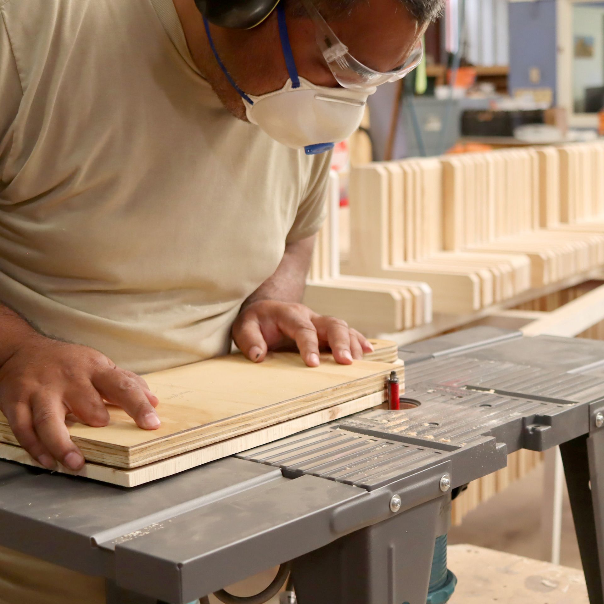 A man wearing a mask is cutting a piece of wood on a table saw