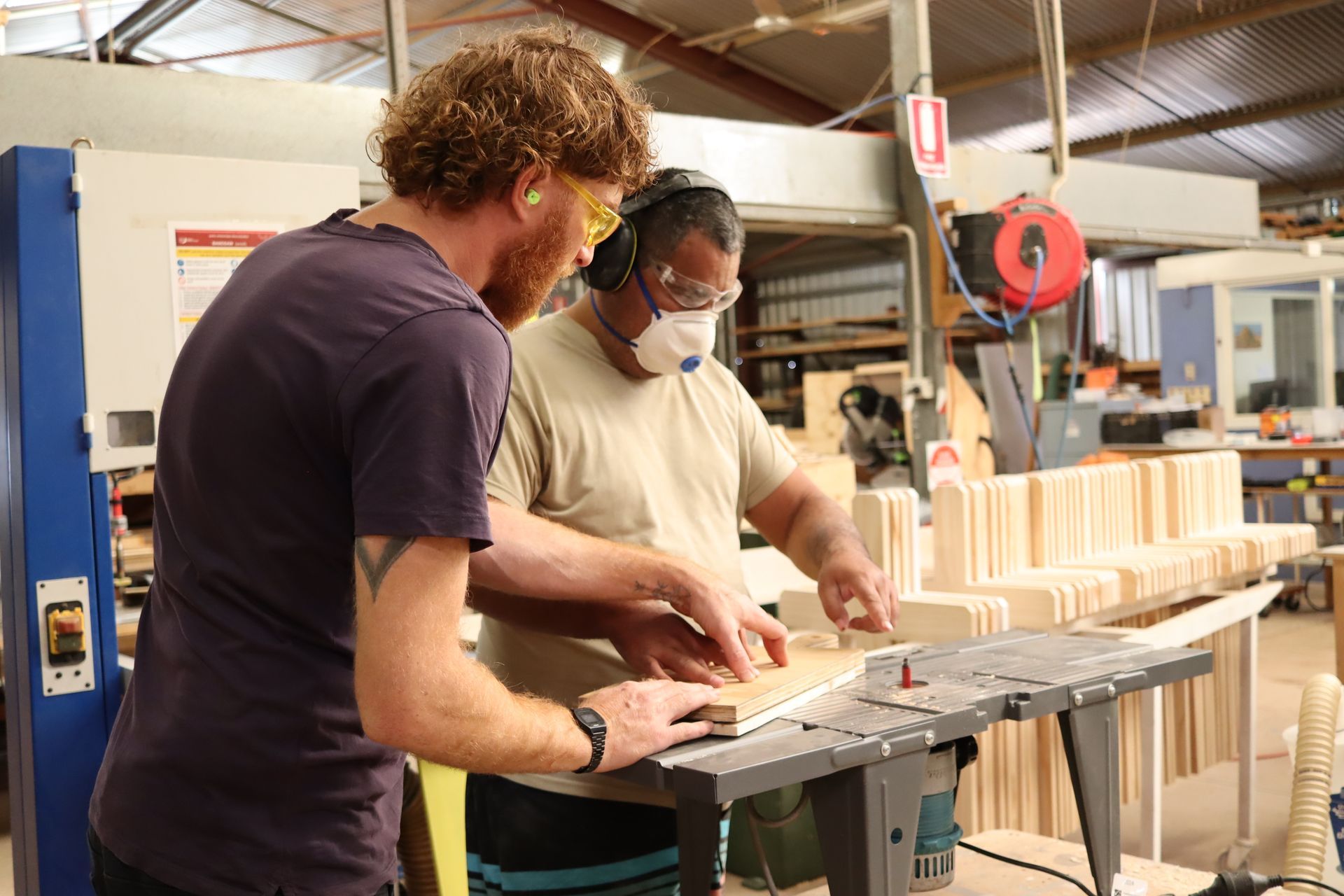 Two men are working on a piece of wood in a factory.