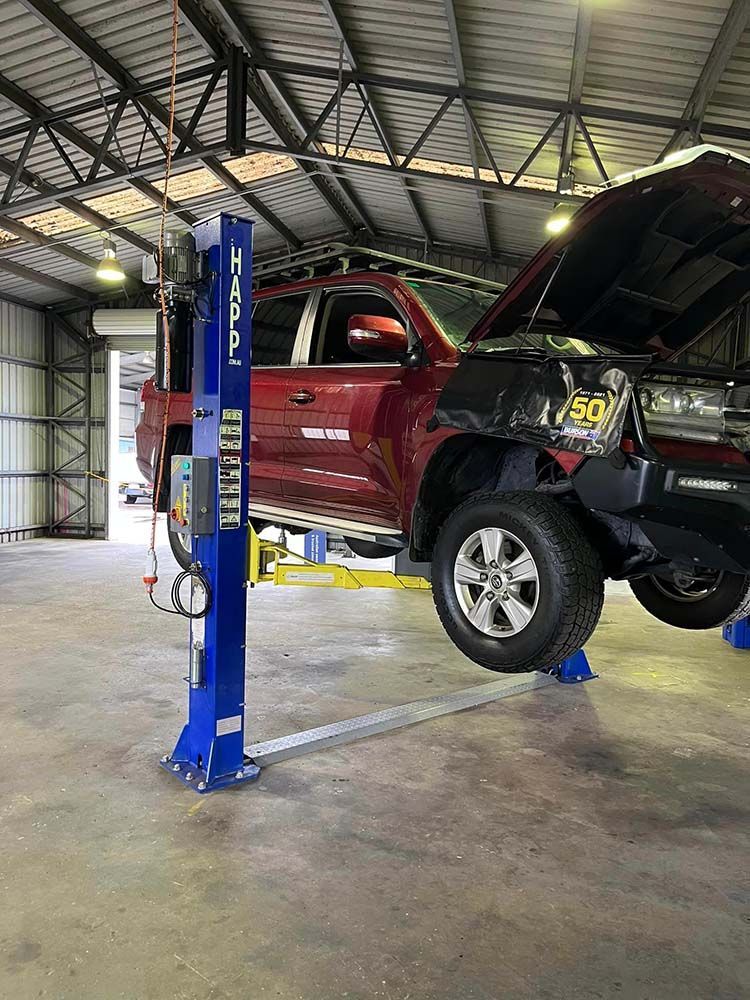 Red Truck On A Lift Inside An Auto Shop. The Hood Is Open. A Blue Lift Is In The Foreground