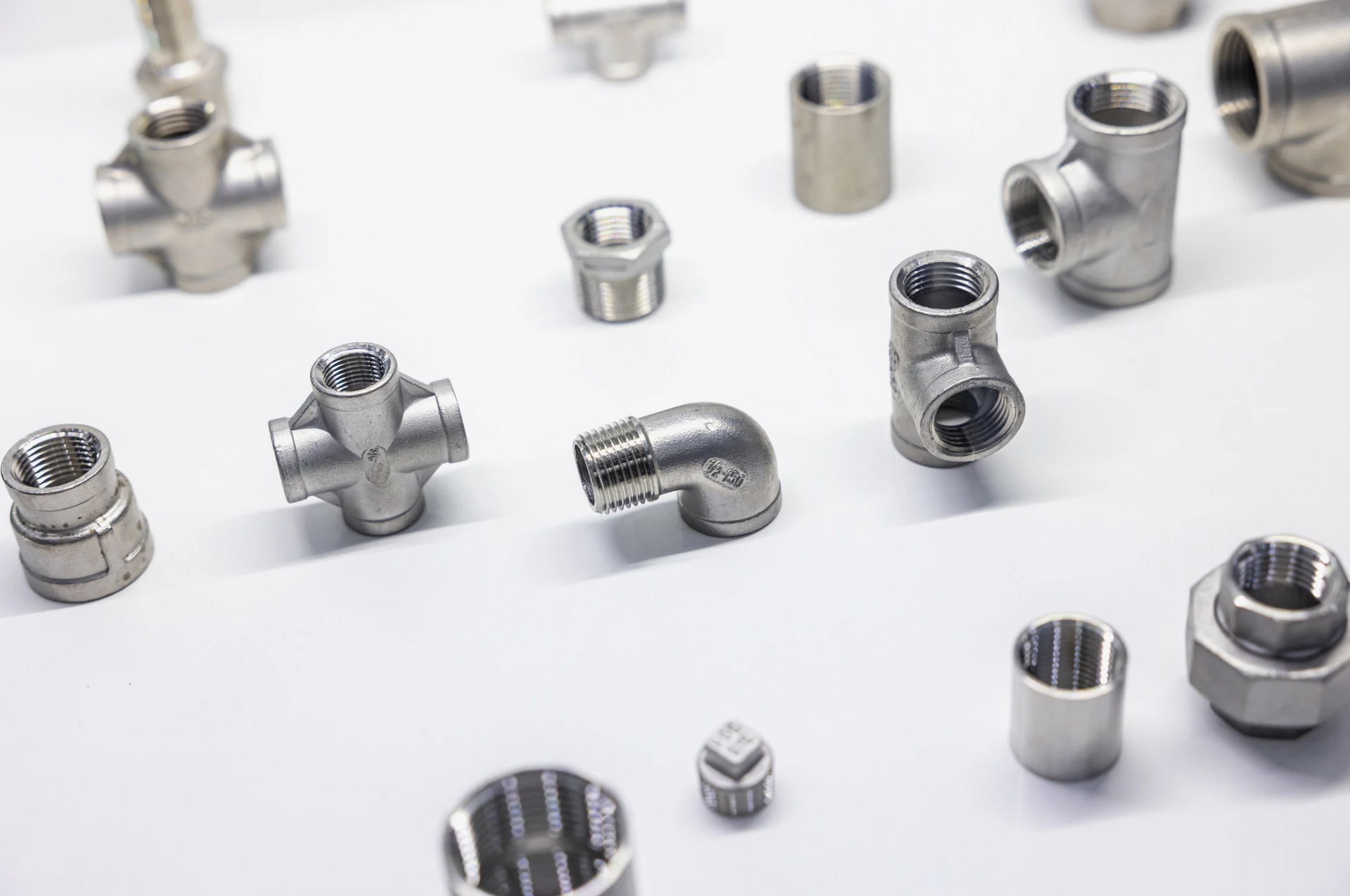 Various stainless steel plumbing fittings on a white surface, including elbows, tees, and couplings.