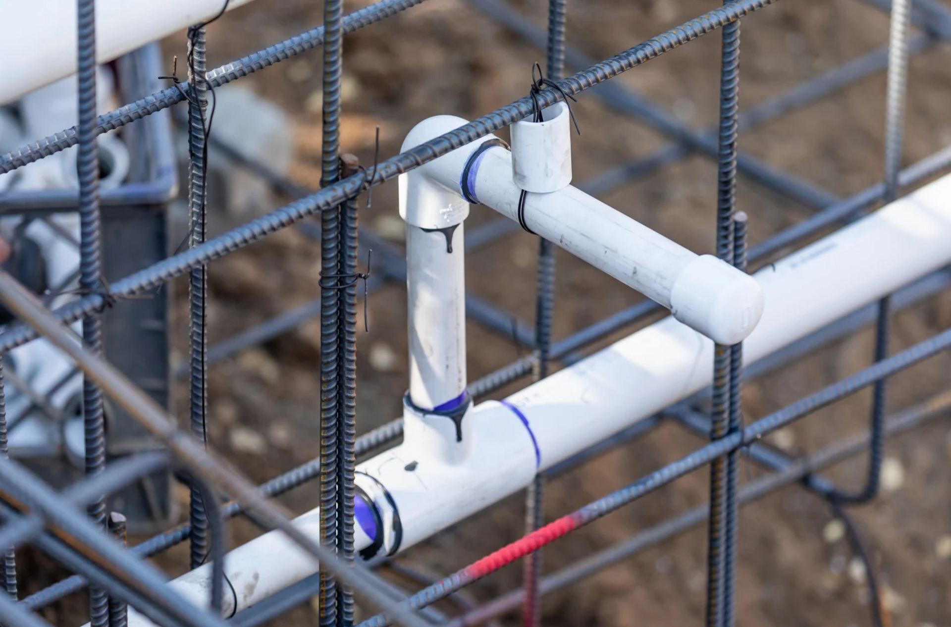 White PVC pipes with joints set within a steel rebar grid, likely for construction.