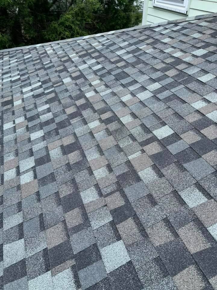 A sloped roof covered in weathered, multi-toned gray and brown asphalt shingles next to a light-colored house wall.