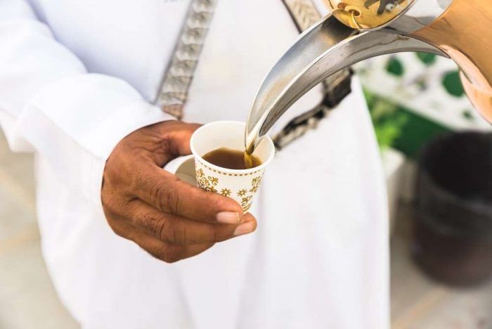 An Emirati host in traditional white kandura serves a glass bowl of luqaimat (sweet dumplings) to in