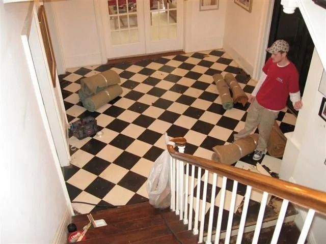 Hallway with black-and-white checkerboard floor, staircase, and a person in a red shirt near the right wall