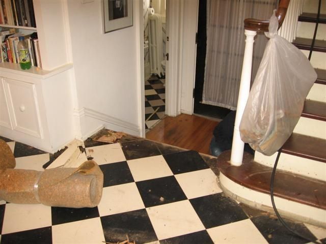 Living room with black-and-white checkered floor, a knocked-over scratching post, and a hanging bag by the stairs