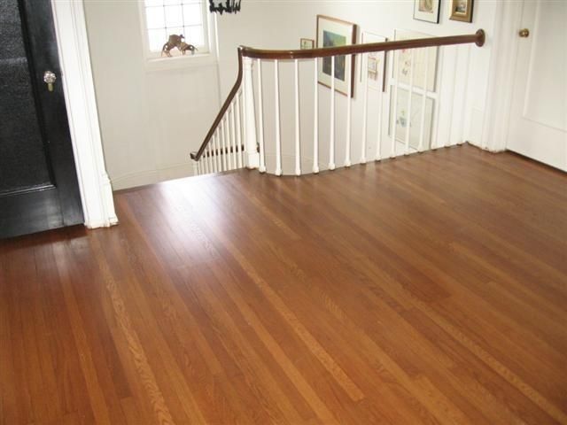 Empty hardwood living room with white railing and a stair landing in the background