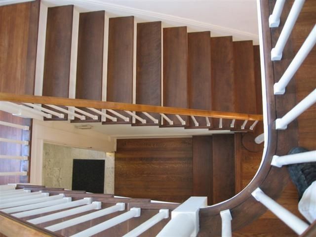 Top-down view of a wooden spiral staircase with white railings and a central stairwell opening