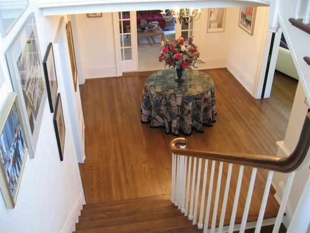 Hallway with hardwood floor, staircase, and round table with a floral centerpiece.