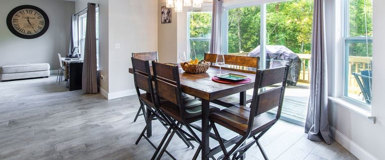 Bright dining room with a wooden table, chairs, wall clock, and large glass doors opening to a patio.