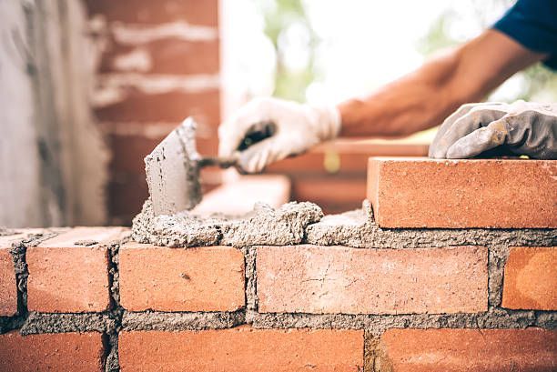 A worker from Excel Chimney & Fireplace is laying brick masonry on an exterior wall in Seattle, WA, 