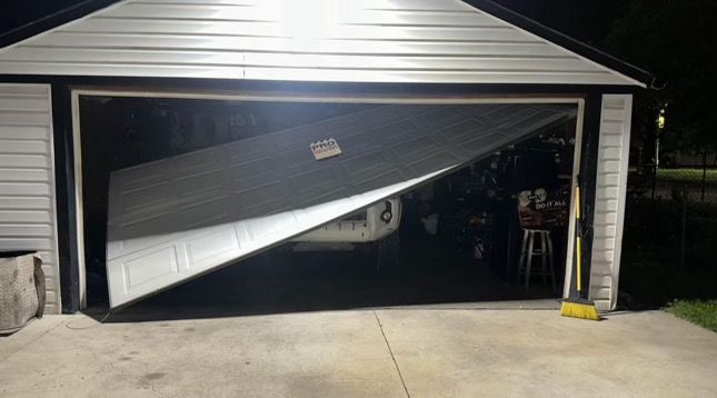 A garage door is broken in half and is open at night.