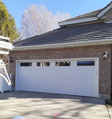A white garage door is sitting in front of a brick house.