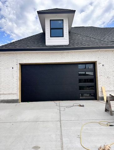 A black garage door is being installed on a white brick house.