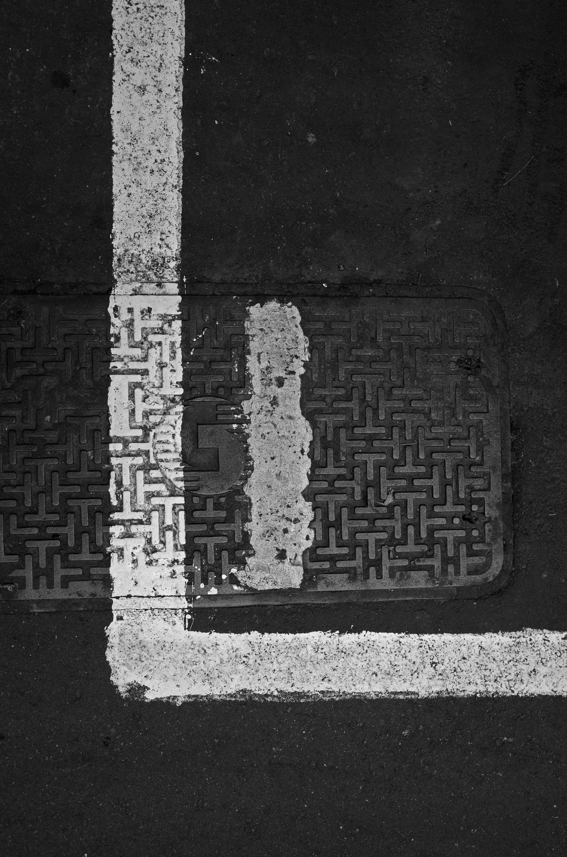 A black and white photo of a manhole cover and a white line
