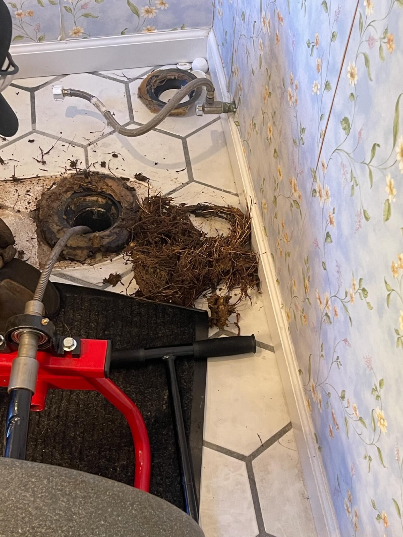 Toilet drain partially disassembled with plumbing tools and debris on tile floor.