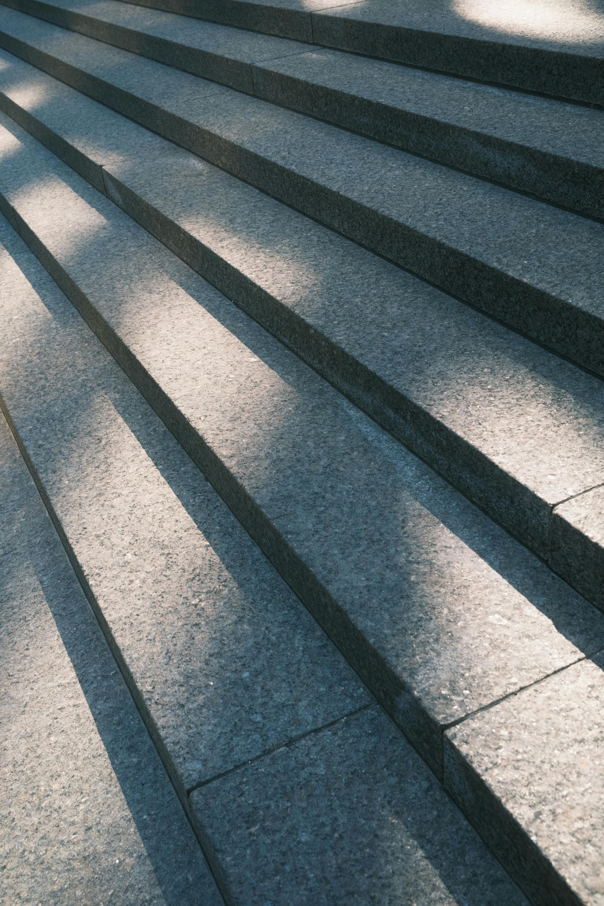 Sunlit stone steps with long diagonal shadows across a textured pavement