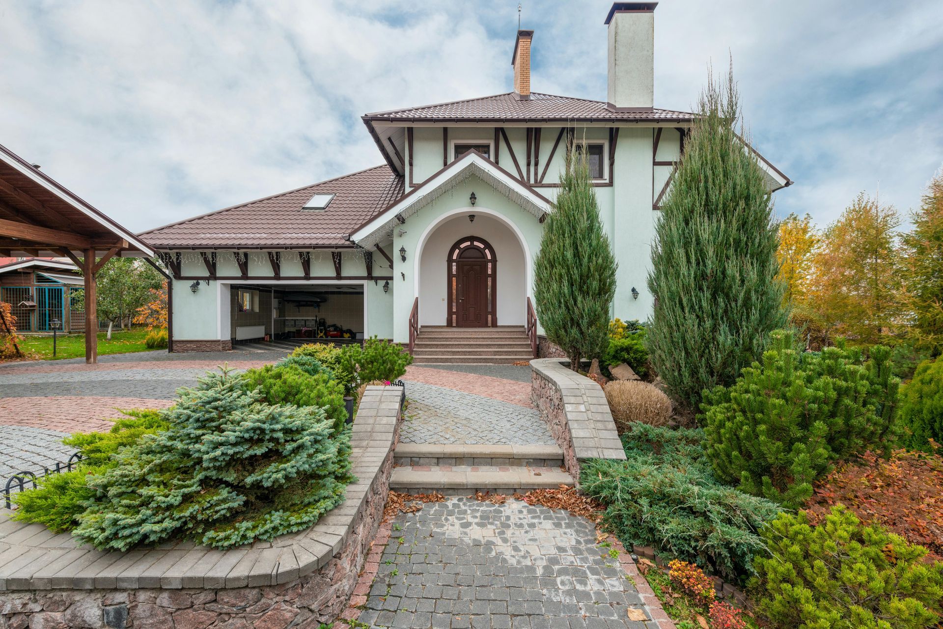 Stone house with arched front door, steps, and landscaped garden under an overcast sky