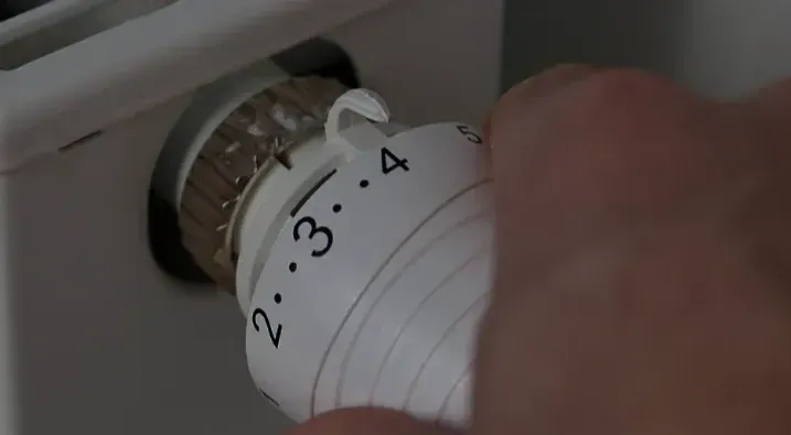 A person is adjusting a thermostat on a radiator.