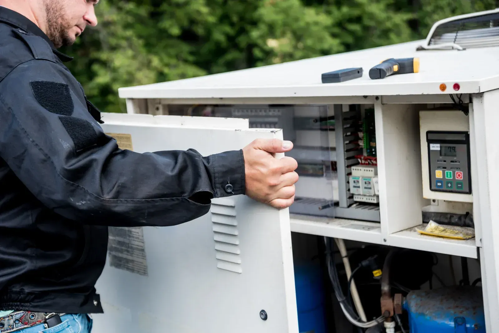 A man in a black jacket is working on an electrical box.