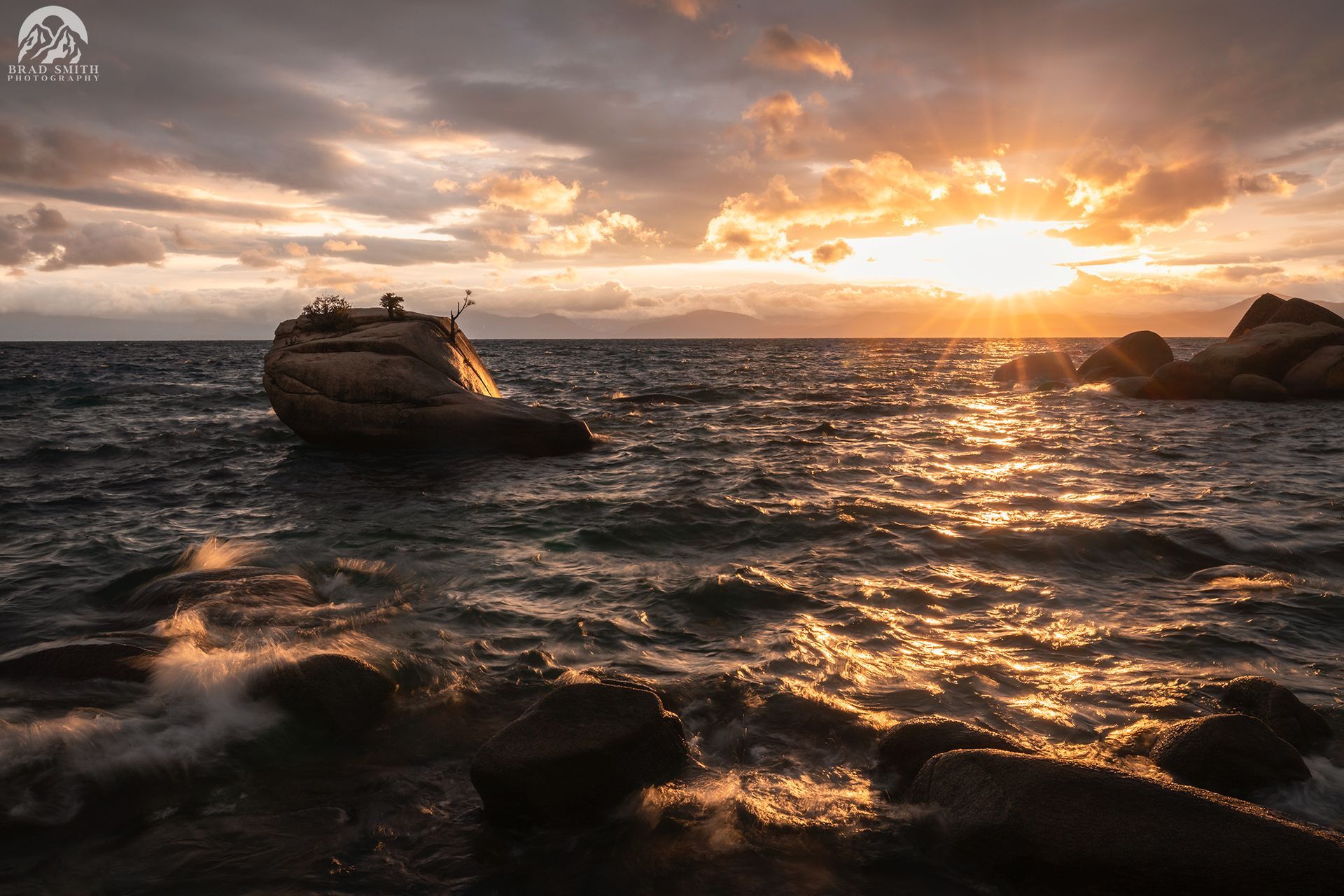Sunset over rocky ocean with a small boat drifting on choppy water.