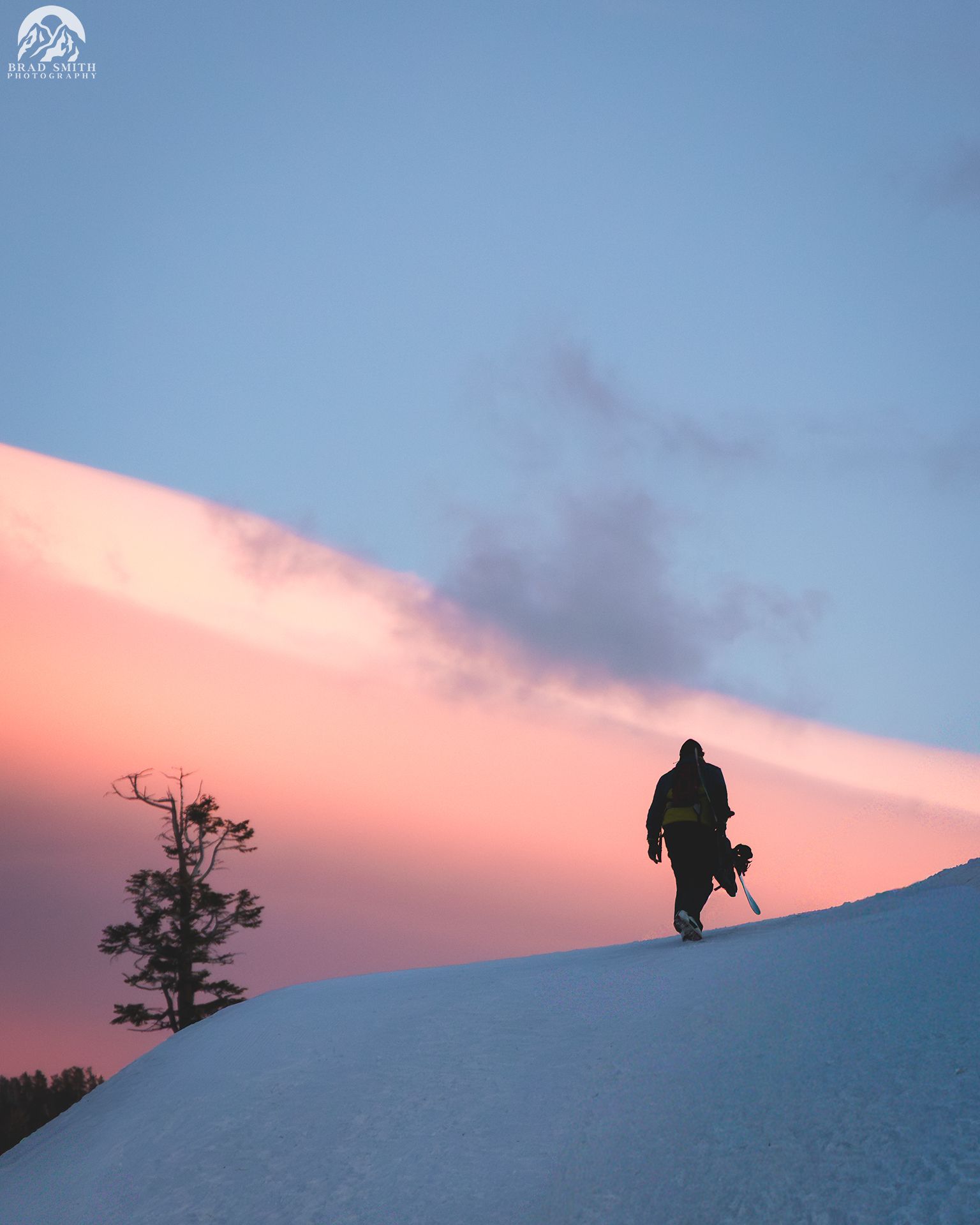 Silhouetted hiker on snowy ridge at sunset under a pink and blue sky