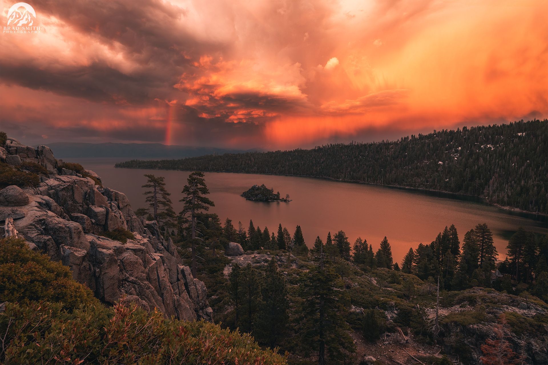 Sunset over a calm lake framed by pine-covered cliffs and orange clouds