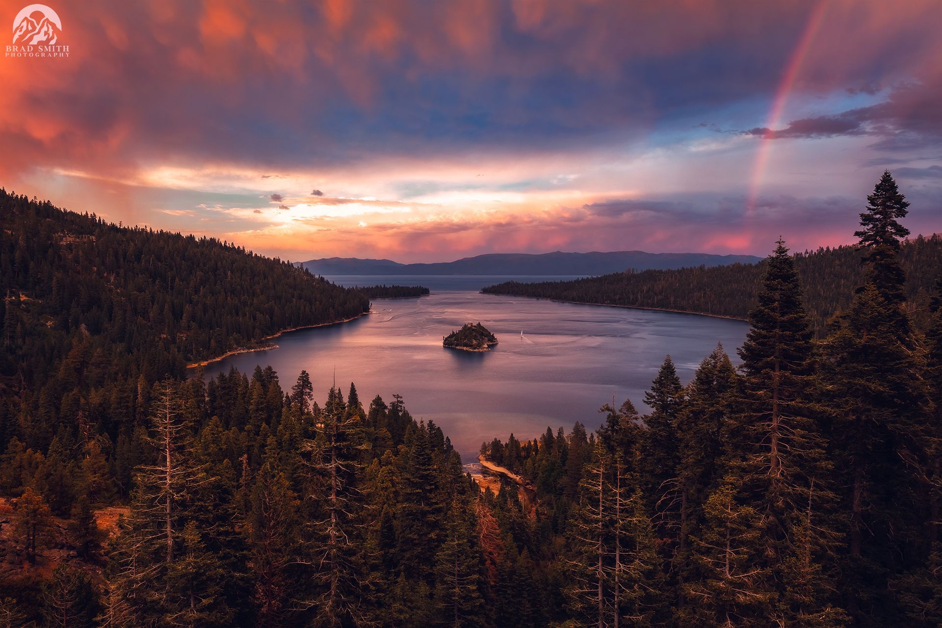 Sunset over a lake with a small island, pine forest, and pink-orange sky