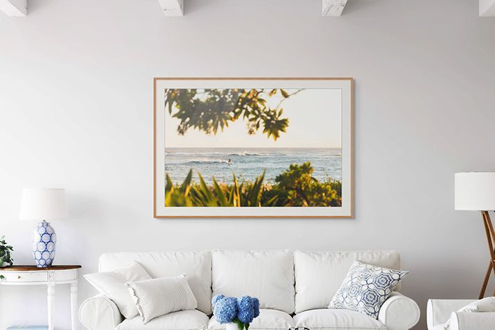 Bright living room with a framed seaside landscape above a white sofa and blue accent pillows
