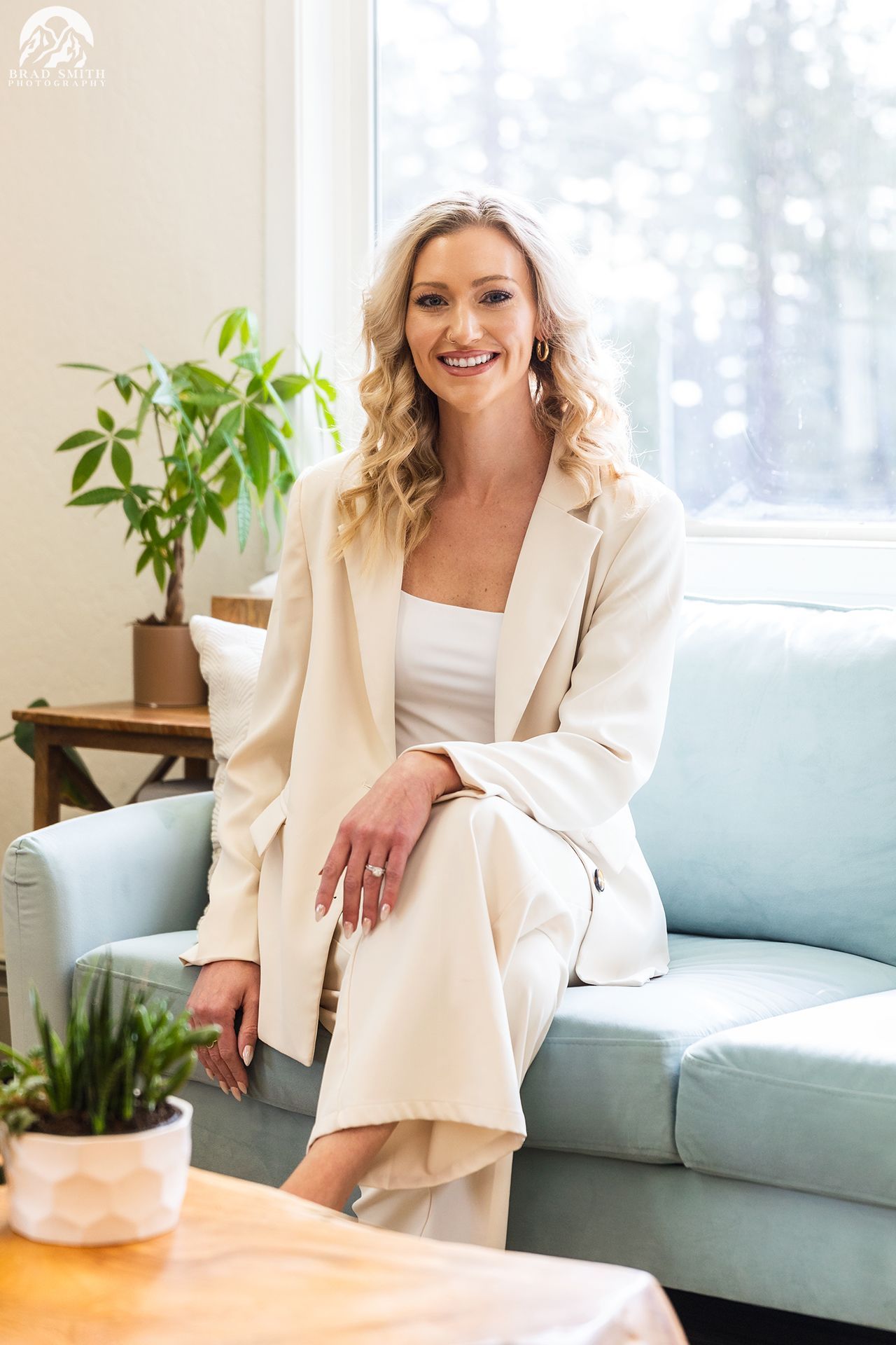 Woman sitting on a light blue sofa in a bright living room with a potted plant and a window behind her